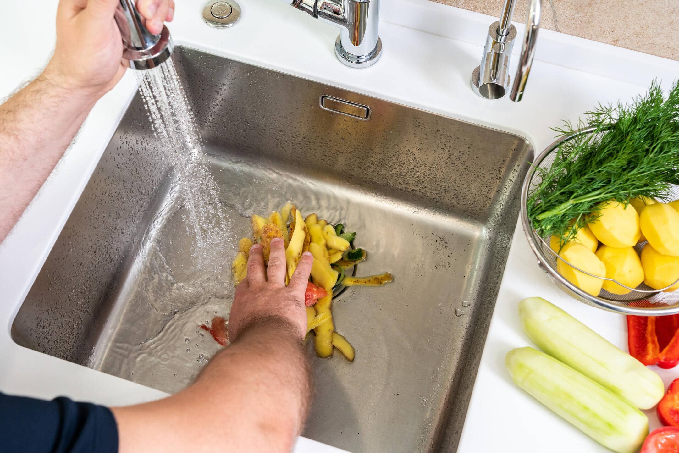 how to unclog garbage disposal-man shoving vegetable peels down a garbage disposal how to unclog garbage disposal-man shoving vegetable peels down a garbage disposal