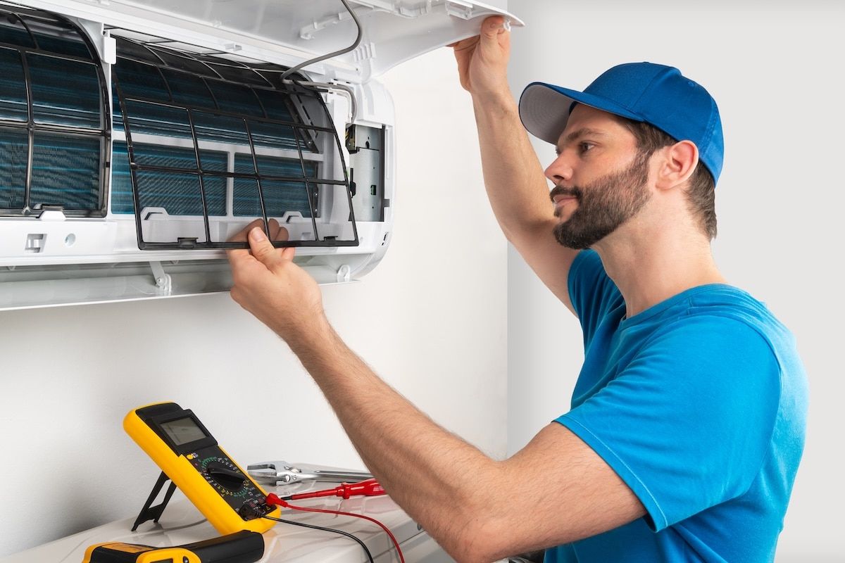 Installation service fix repair maintenance of an air conditioner indoor unit, by cryogenist technican worker checking the air filter in blue shirt and baseball cap Installation service fix repair maintenance of an air conditioner indoor unit, by cryogenist technican worker checking the air filter in blue shirt and baseball cap