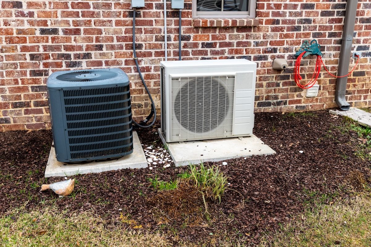 HVAC Air Conditioner Compressor and a Mini-split system together next to each other, next to a brick home. HVAC Air Conditioner Compressor and a Mini-split system together next to each other, next to a brick home.