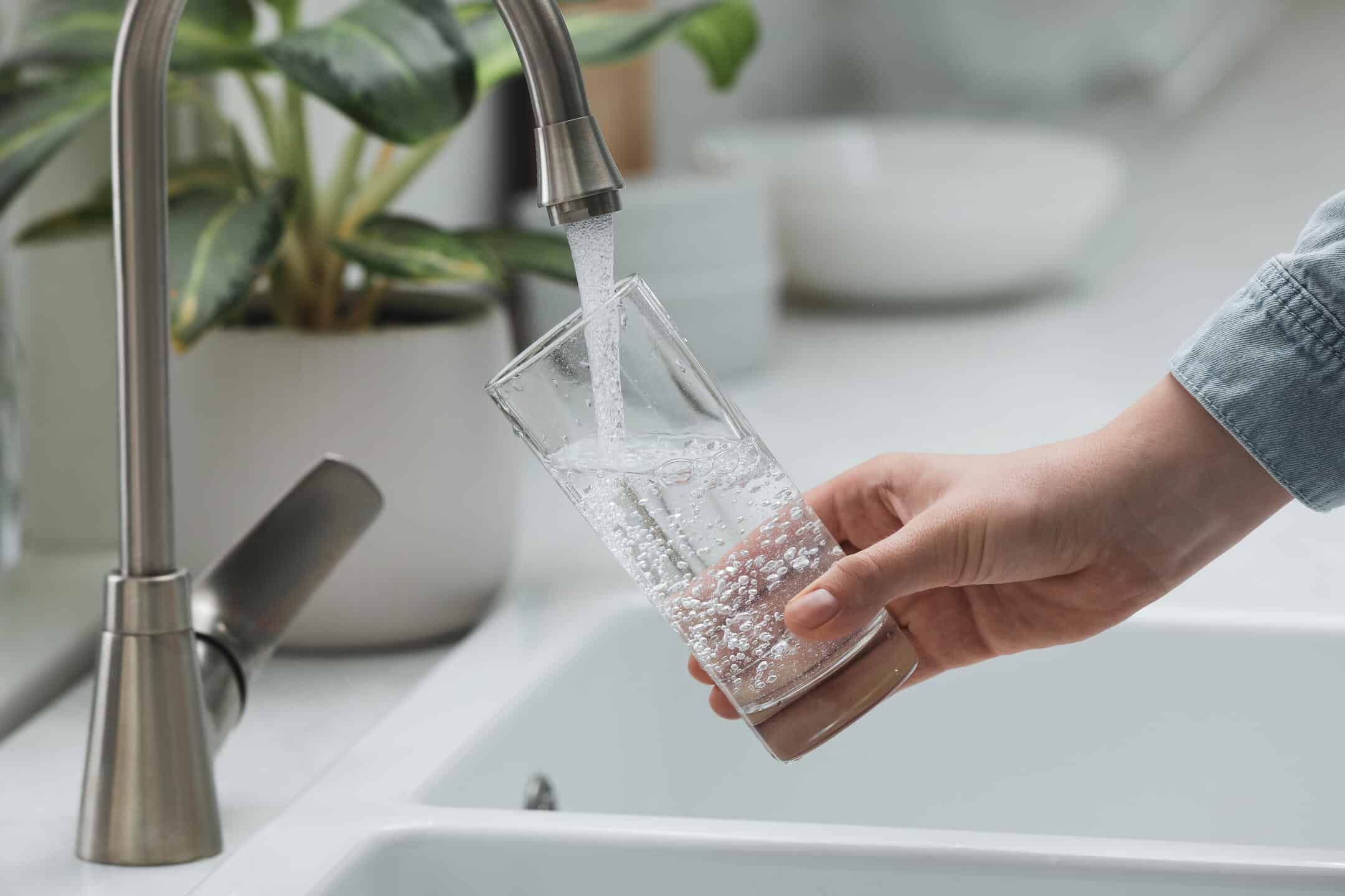 best under sink water filter-woman filling up a drinking glass with water from the kitchen faucet best under sink water filter-woman filling up a drinking glass with water from the kitchen faucet