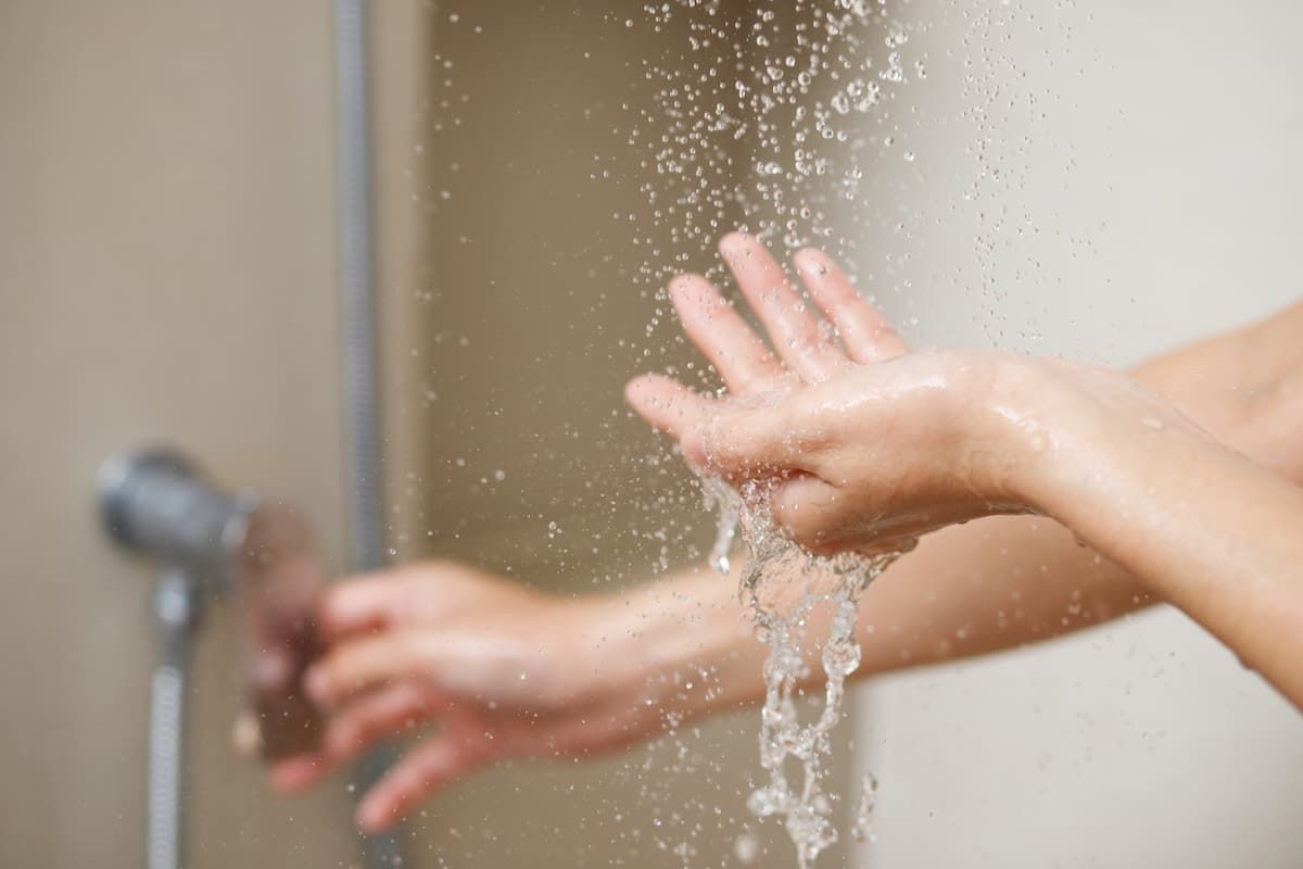 A woman uses hand to measure the water temperature from a water heater before taking a shower A woman uses hand to measure the water temperature from a water heater before taking a shower