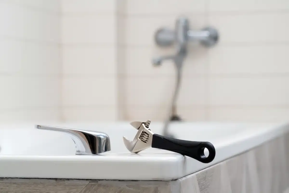 hand tool resting on a bathtub ledge next to bathtub parts hand tool resting on a bathtub ledge next to bathtub parts
