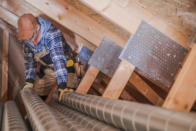 central air installation-technician working with ductwork in a house attic