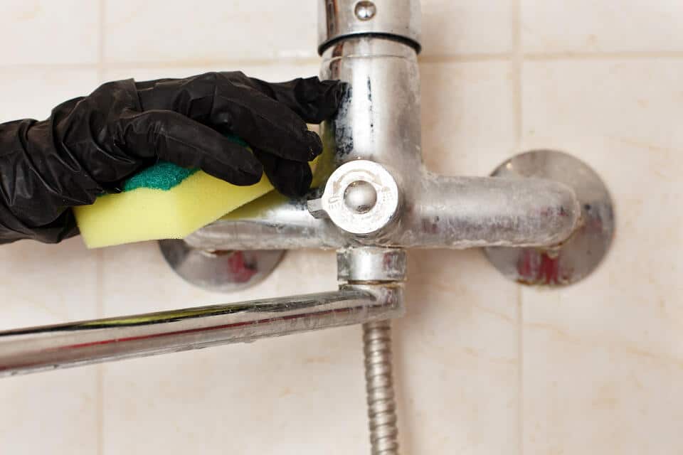 signs of hard water-gloved hand trying to remove hard water stains from shower faucet