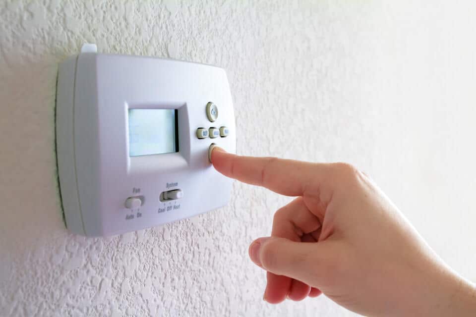 thermostat not working-close up of hand adjusting a wall thermostat