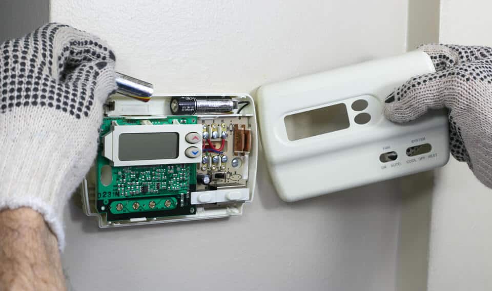 thermostat not working-gloved hands replacing batteries on a wall thermostat