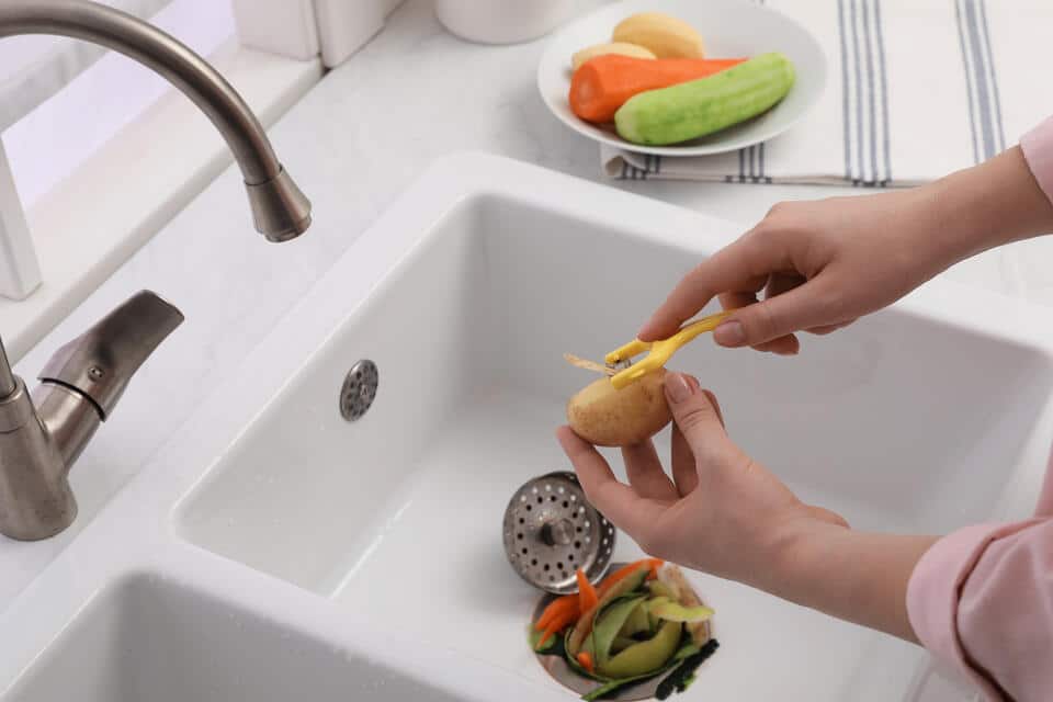 how to unclog garbage disposal-woman peeling vegetables directly into a garbage disposal