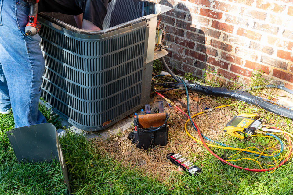 ac tune up cost-technician inspecting an outdoor AC unit