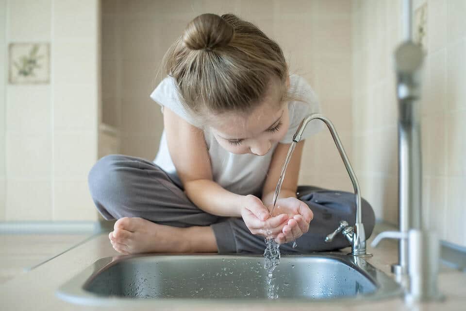 best under sink water filter-young girl drinking water from a water spigot in the kitchen sink