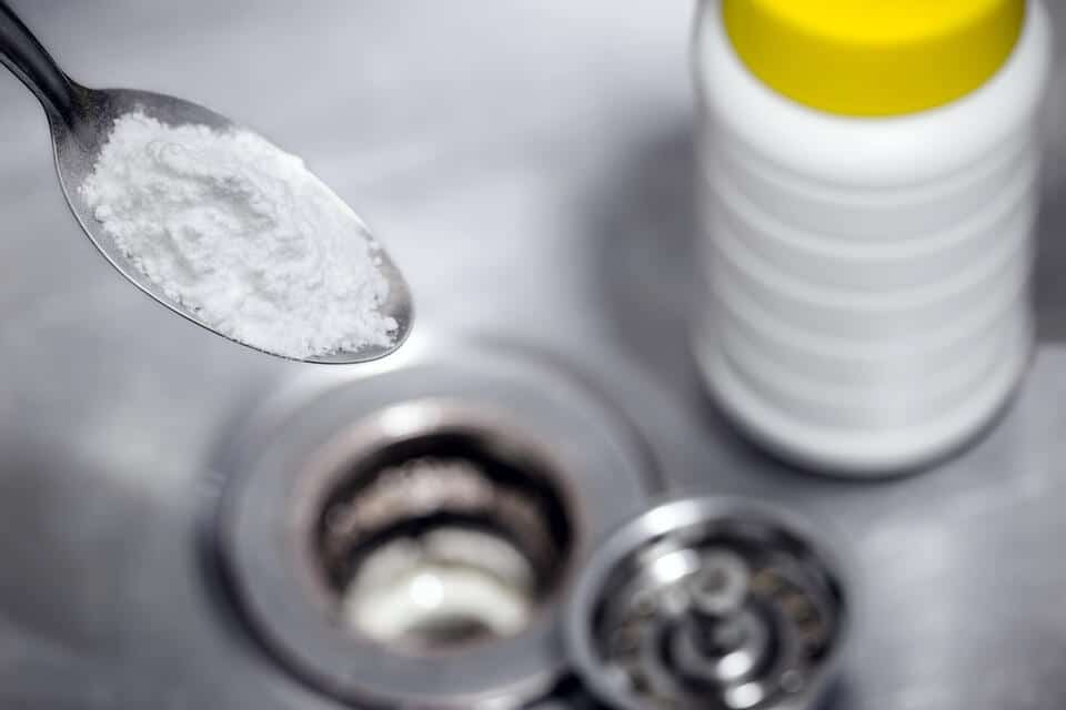 how to unclog sink-close up of a person using baking soda and vinegar to unclog a kitchen sink