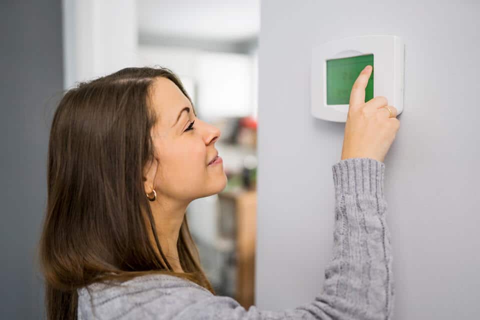 hvac refrigerant-woman in gray sweater adjusting the thermostat