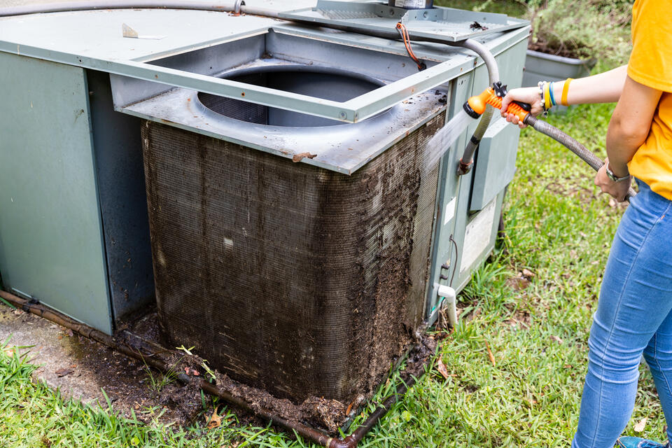 ac maintenance cost-person hosing off coils of central AC unit outside