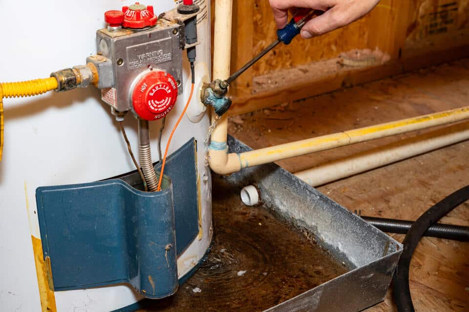hot water heater leaking-man closing valve on water heater with screw driver