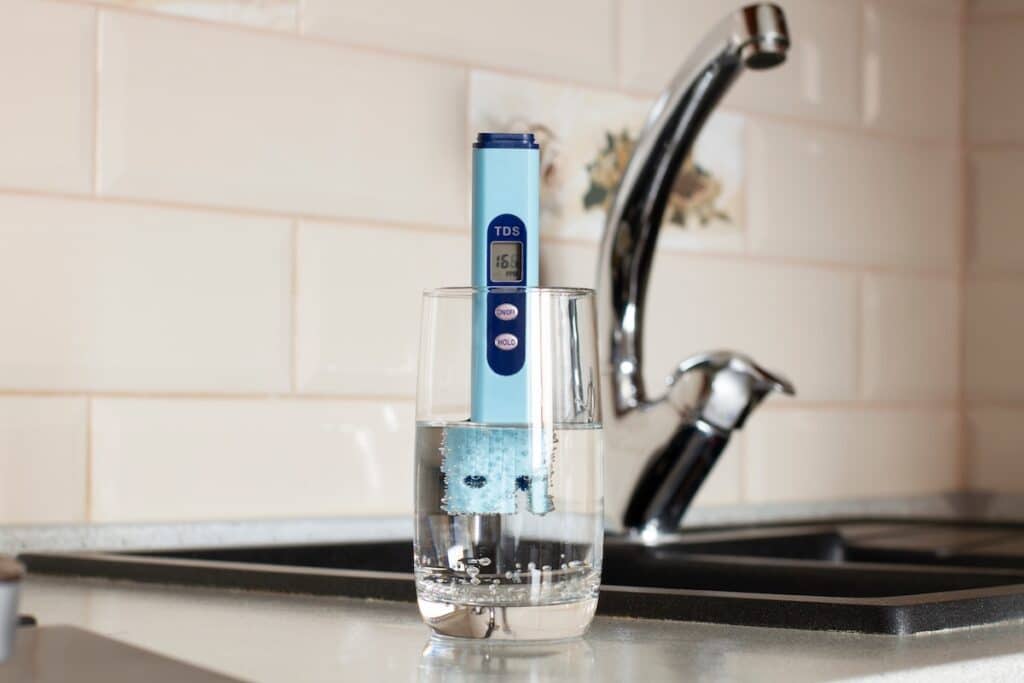TDS measurement of water. Electronic pH meter in a glass of water. In the background there is a tap for drinking water. The concept of testing water for miralization