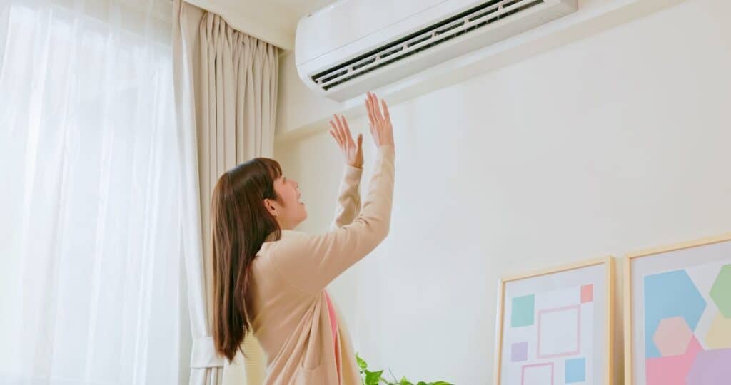 asian woman turn on heater and feel warm in winter standing at home