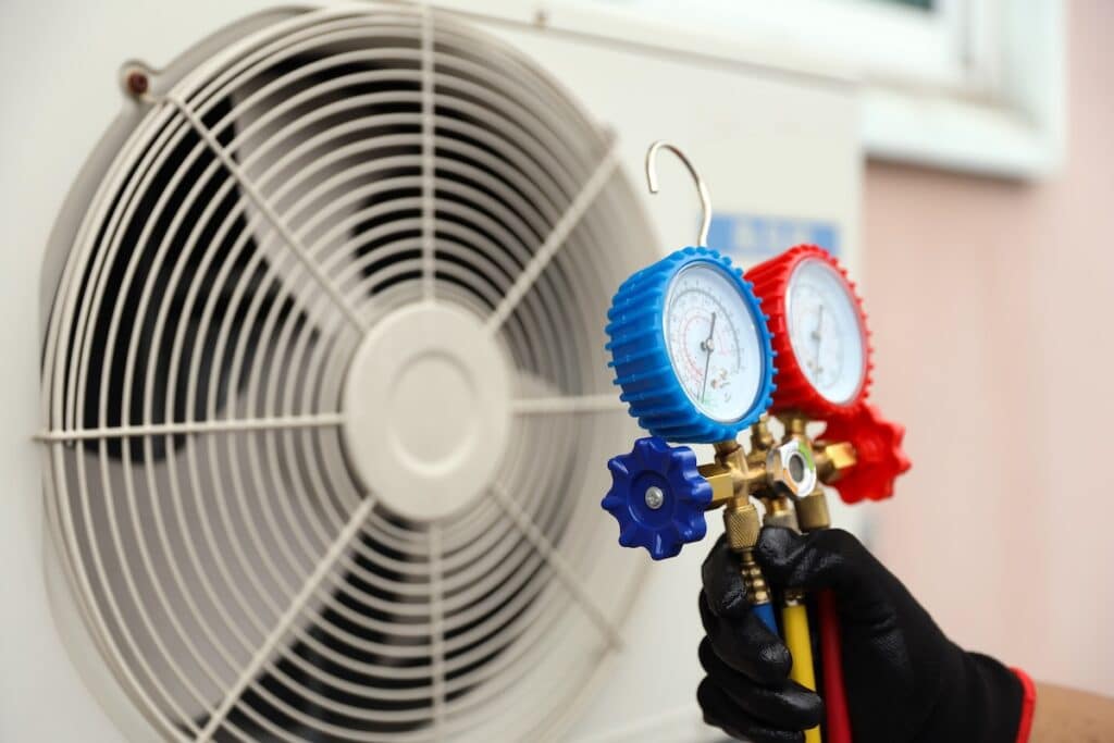 Electrical technician conditioning using manifold gauge measuring tool checking refrigerant pump filling home air conditioner and maintenance heat fix repair and clean outdoor air compressor unit.