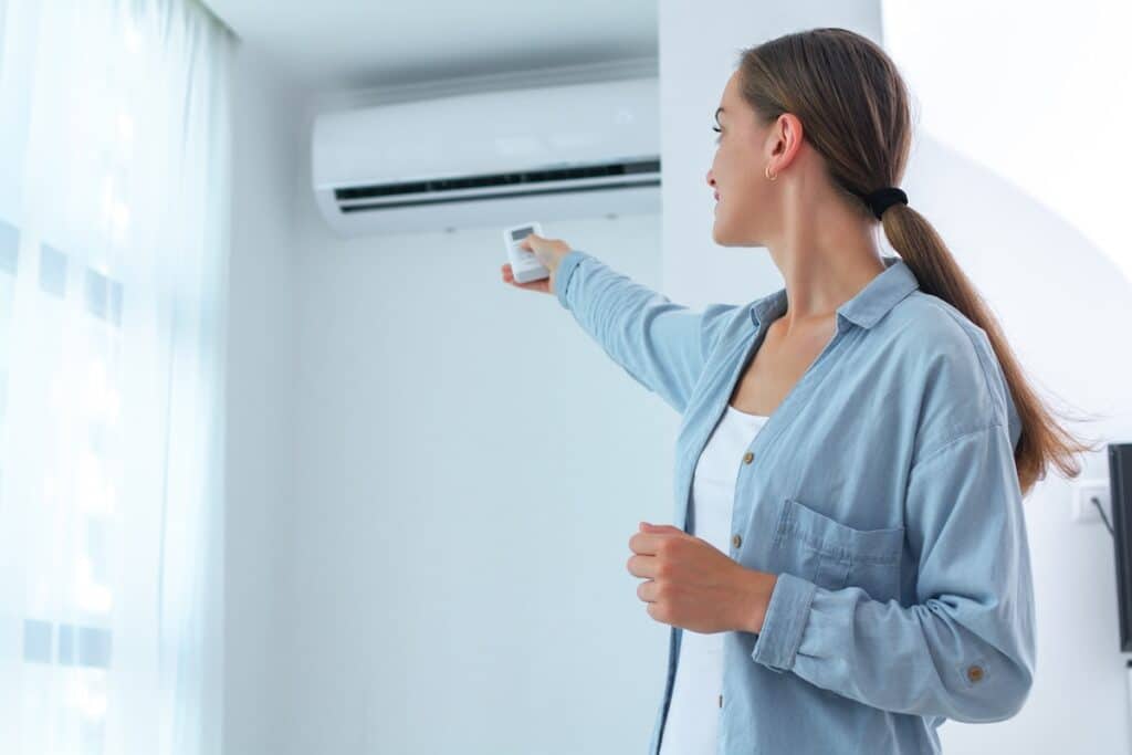 Young woman adjusts the temperature of the air conditioner using the remote control in room at home what is btu in ac
