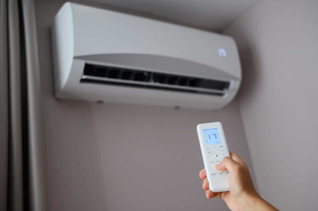 Man's hand holds air conditioner remote control and sets cooling temperature on split system to 17 degrees. Concept of air cooling in heat of room, climate control at home