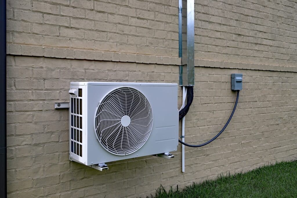 Air Conditioner mini split system next to home with painted brick wall and space for text copy