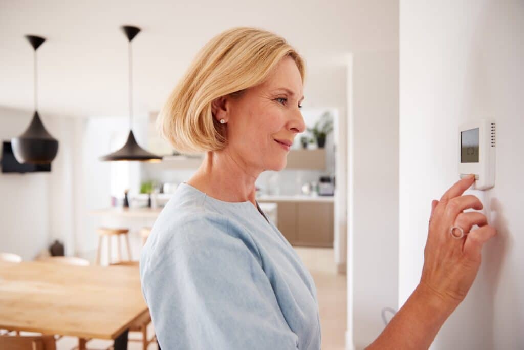 hvac zoning system Close Up Of Mature Woman Adjusting Central Heating Temperature At Home On Thermostat